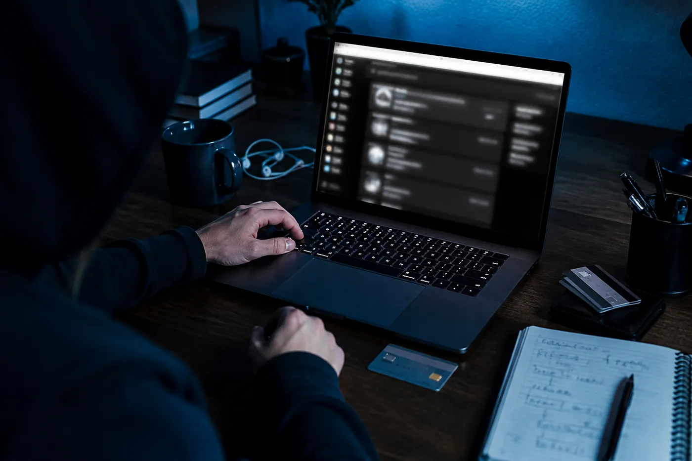 A person focused on navigating a dark web carding forum on their laptop in a dimly lit room.